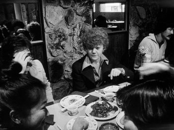 Movie still from “Chan Is Missing” (1982), directed by Wayne Wang – An older woman sitting at a table with a plate of food in front of her; Medium shot, Over the shoulder angle
