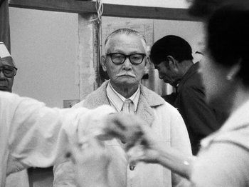Movie still from “Chan Is Missing” (1982), directed by Wayne Wang – An older man wearing glasses and a white coat; Medium shot, Low angle