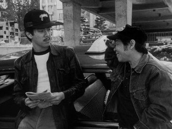 Movie still from “Chan Is Missing” (1982), directed by Wayne Wang – Two men are talking to each other in a parking lot; Medium shot, Low angle