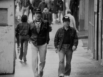 Movie still from “Chan Is Missing” (1982), directed by Wayne Wang – A couple of men walking down a sidewalk; Medium shot, Low angle