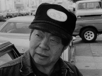 Movie still from “Chan Is Missing” (1982), directed by Wayne Wang – An older man wearing a hat in a parking lot; Close Up shot, Low angle