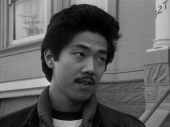 Movie still from “Chan Is Missing” (1982), directed by Wayne Wang – Black and white photograph of a young man with a mustache; Close Up shot, Low angle