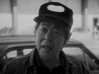Movie still from “Chan Is Missing” (1982), directed by Wayne Wang – An older man wearing a hat standing in front of a car; Close Up shot, Low angle