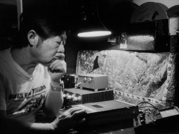 Movie still from “Chan Is Missing” (1982), directed by Wayne Wang – A man sitting in front of a computer monitor; Medium shot, Low angle