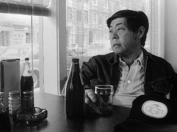 Movie still from “Chan Is Missing” (1982), directed by Wayne Wang – An older man sitting at a table with a glass of beer; Close Up shot, Low angle