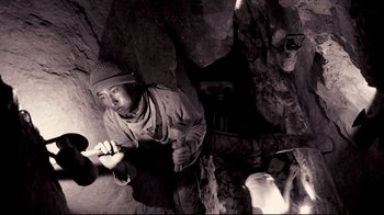 Movie still from “Che: Part Two” (2008), directed by Steven Soderbergh – A man in a hat is climbing a rock wall; Medium shot, Low angle