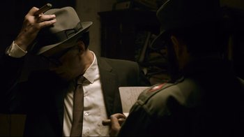 Movie still from “Che: Part Two” (2008), directed by Steven Soderbergh – A man in a suit and a hat is looking at a paper; Medium shot, Over the shoulder angle