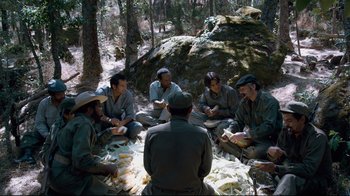 Movie still from “Che: Part Two” (2008), directed by Steven Soderbergh – A group of men sitting around a forest; Wide shot, High angle