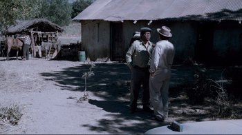 Movie still from “Che: Part Two” (2008), directed by Steven Soderbergh – Two men standing in front of an old house; Wide shot, Over the shoulder angle