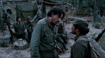 Movie still from “Che: Part Two” (2008), directed by Steven Soderbergh – A group of men sitting in the woods talking to each other; Medium shot, Over the shoulder angle