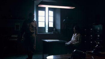 Movie still from “Che: Part Two” (2008), directed by Steven Soderbergh – Two men are sitting at a table in a dark room; Wide shot, Over the shoulder angle