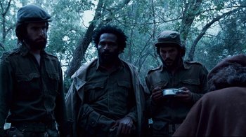 Movie still from “Che: Part Two” (2008), directed by Steven Soderbergh – A group of men standing next to each other in the woods; Medium shot, Over the shoulder angle