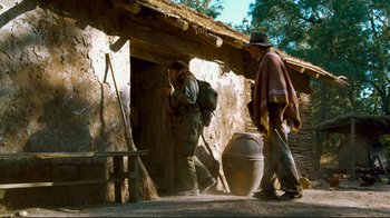 Movie still from “Che: Part Two” (2008), directed by Steven Soderbergh – Two men walking in front of an adobe building; Wide shot, Low angle
