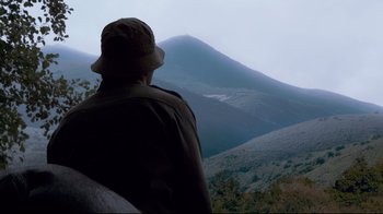 Movie still from “Che: Part Two” (2008), directed by Steven Soderbergh – A man wearing a hat looking out at a mountain; Medium shot, Low angle