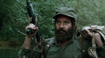 Movie still from “Che: Part Two” (2008), directed by Steven Soderbergh – A man with a beard holding a rifle in a forest; Close Up shot, Low angle