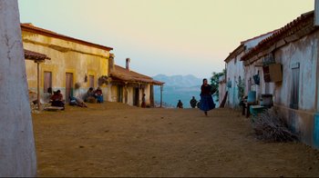 Movie still from “Che: Part Two” (2008), directed by Steven Soderbergh – A woman walking down a dirt road near a mountain; Extreme Wide shot, Low angle