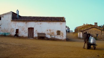 Movie still from “Che: Part Two” (2008), directed by Steven Soderbergh – An old white building with a bench in front of it; Extreme Wide shot, Low angle