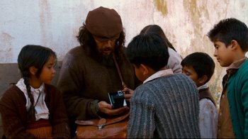 Movie still from “Che: Part Two” (2008), directed by Steven Soderbergh – A man is looking at his cell phone while others look on; Medium shot, High angle