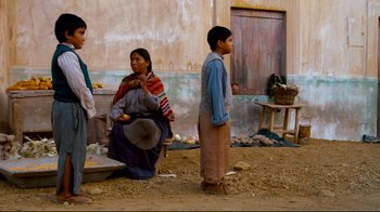 Movie still from “Che: Part Two” (2008), directed by Steven Soderbergh – A woman and two boys standing in a dirt field; Wide shot, Over the shoulder angle