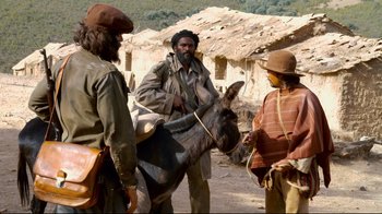 Movie still from “Che: Part Two” (2008), directed by Steven Soderbergh – A man and two men standing next to a donkey on a dirt road; Medium shot, Over the shoulder angle
