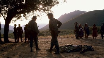 Movie still from “Che: Part Two” (2008), directed by Steven Soderbergh – A group of men standing around a dead body in a field; Wide shot, Over the shoulder angle