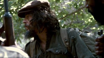 Movie still from “Che: Part Two” (2008), directed by Steven Soderbergh – A man with long hair and a beard wearing a hat; Close Up shot, Over the shoulder angle