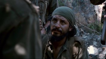 Movie still from “Che: Part Two” (2008), directed by Steven Soderbergh – A man with a beard and a green turban is in the woods; Close Up shot, Over the shoulder angle