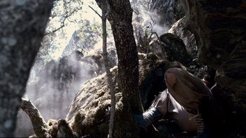 Movie still from “Che: Part Two” (2008), directed by Steven Soderbergh – A person is sitting on a rock near a tree; Wide shot, Low angle