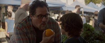 Movie still from “Chef” (2014), directed by Jon Favreau – A man holding an orange in front of a child; Close Up shot, Over the shoulder angle