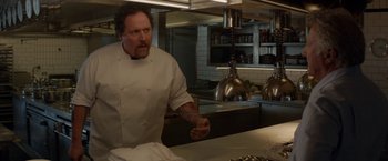 Movie still from “Chef” (2014), directed by Jon Favreau – A man standing in a kitchen preparing a meal; Medium shot, Over the shoulder angle