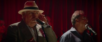 Movie still from “Chef” (2014), directed by Jon Favreau – An older man wearing a hat is singing into a microphone; Close Up shot, Over the shoulder angle