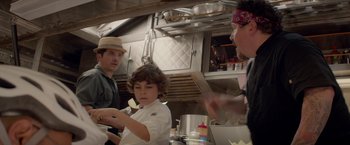 Movie still from “Chef” (2014), directed by Jon Favreau – A man and a boy in a kitchen preparing food; Medium shot, Over the shoulder angle