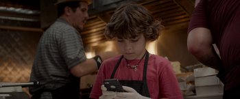 Movie still from “Chef” (2014), directed by Jon Favreau – A young boy wearing an apron looking at a cell phone; Close Up shot, High angle