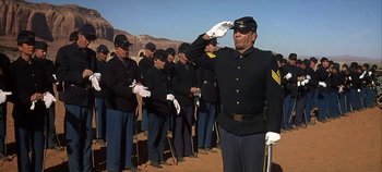 Movie still from “Cheyenne Autumn” (1964), directed by John Ford – A group of men in uniform saluting in the desert; Medium shot, Low angle