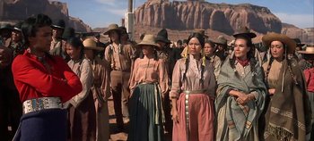 Movie still from “Cheyenne Autumn” (1964), directed by John Ford – A group of people standing next to each other on a dirt road; Wide shot, Low angle