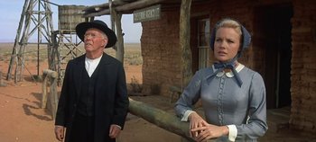 Movie still from “Cheyenne Autumn” (1964), directed by John Ford – An older man and woman standing next to a wooden fence; Medium shot, Low angle