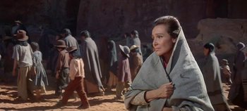 Movie still from “Cheyenne Autumn” (1964), directed by John Ford – A woman holding an umbrella while standing in front of a group of people; Medium shot, Over the shoulder angle