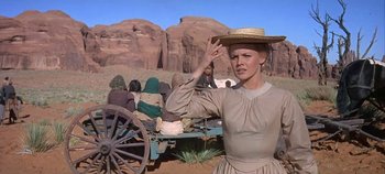 Movie still from “Cheyenne Autumn” (1964), directed by John Ford – A woman with a straw hat standing next to a wagon; Medium shot, Over the shoulder angle