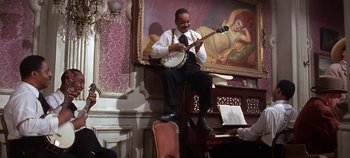 Movie still from “Cheyenne Autumn” (1964), directed by John Ford – A man sitting on top of a chair holding a banjo; Wide shot, Low angle