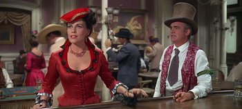 Movie still from “Cheyenne Autumn” (1964), directed by John Ford – A woman in a red dress sitting at a bar; Medium shot, Over the shoulder angle