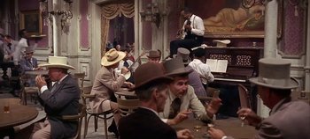 Movie still from “Cheyenne Autumn” (1964), directed by John Ford – A group of men sitting at a table in front of a piano; Wide shot, High angle