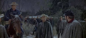 Movie still from “Cheyenne Autumn” (1964), directed by John Ford – An old man wearing a hat walking in the snow with a group of men; Medium shot, Low angle