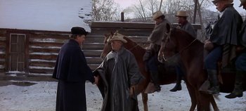 Two men are shaking hands in front of two horses