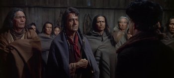 Movie still from “Cheyenne Autumn” (1964), directed by John Ford – A group of people standing in front of a wooden wall; Medium shot, Over the shoulder angle