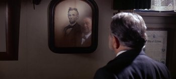 Movie still from “Cheyenne Autumn” (1964), directed by John Ford – A man in a suit looking at an image of abraham lincoln in a mirror; Close Up shot, Over the shoulder angle