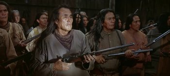 Movie still from “Cheyenne Autumn” (1964), directed by John Ford – Two native american men holding guns in a crowd of people; Medium shot, Low angle