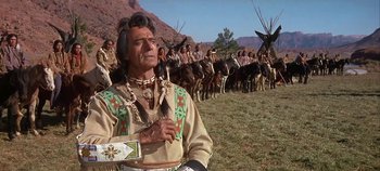 Movie still from “Cheyenne Autumn” (1964), directed by John Ford – An old man in a native american outfit standing in front of a herd of horses; Medium shot, Low angle