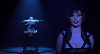 Movie still from “Chicago” (2002), directed by Rob Marshall – A woman standing in front of two men in a dark room; Medium shot, Over the shoulder angle