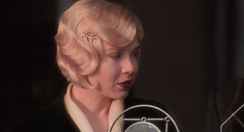 Movie still from “Chicago” (2002), directed by Rob Marshall – A woman with blonde curly hair is holding a microphone in front of her face; Close Up shot, Over the shoulder angle