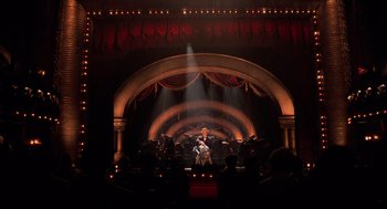 Movie still from “Chicago” (2002), directed by Rob Marshall – A man sitting on a stage in front of an audience; Extreme Wide shot, Low angle